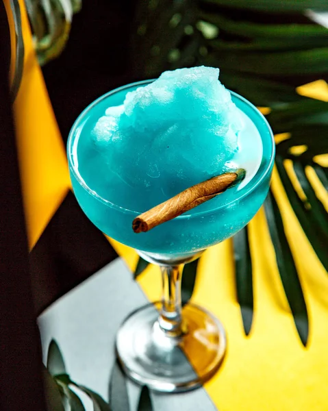 a glass of blue lagoon with ice shaving and cinnamon stick