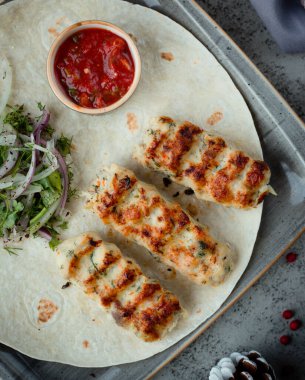 Kızarmış tavuk lula kebabı, soğan salatası ve domates sosuyla servis ediliyor.