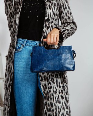 Kot pantolonlu kadın, siyah bluz ve leopar desenli hırka, elinde lacivert çanta.