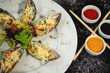 rendelenmiş peynir ve marulla süslenmiş midye tabağı.