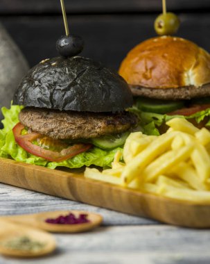 Siyah burger ve kızarmış patatesle servis edilen beyaz hamburger.