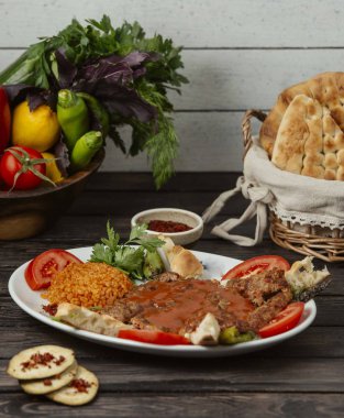 Domates dilimiyle süslenmiş biftek kebabı, bulguru, ekmek ve sebzeyle servis ediliyor.