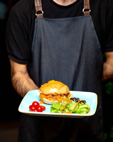 waiter holding burger plate with green salad
