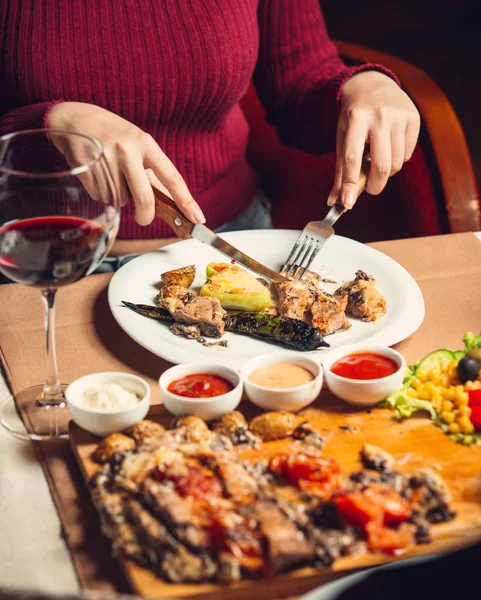 Frau schneidet gegrilltes Hühnersteak mit gegrillter Paprika, Salat und Wein — Stockfoto