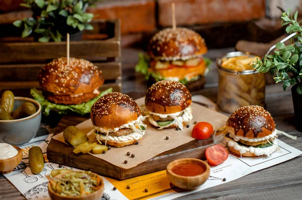 Tre mini nötkött hamburgare och två stora hamburgare serveras med såser och pickles — Stockfoto