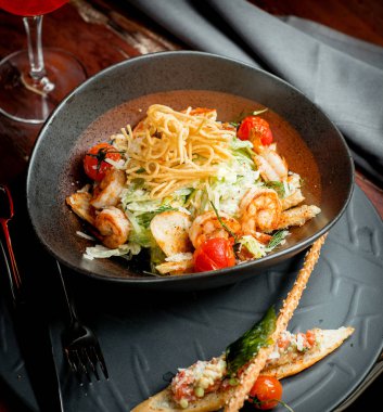 Patates bağcıklarıyla kaplı bir kase karides sezar salatası.