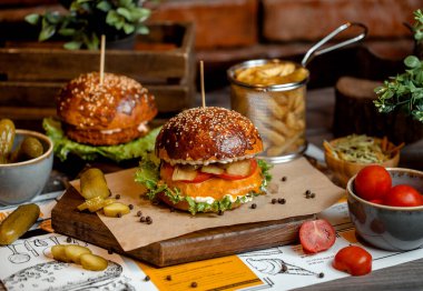 Salatalık turşusu, vişneli domates ve patates kızartmasıyla servis edilen çedarlı biftek burgeri.