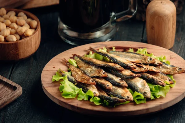 Dried smoked sprat layered on lettuce leaves served on round wood platter — Stock Photo, Image