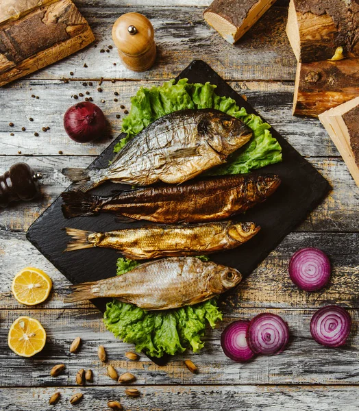 Blick von oben auf geräucherten Fisch mit Salat auf schwarzem Servierbrett — Stockfoto
