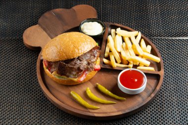 Kızarmış patatesle servis edilen etli biftek, biber turşusu, mayonez ve ketçap.