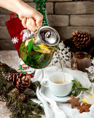 Naneli zencefilli çay dolduran kadın limon ve bal bırakır fincana