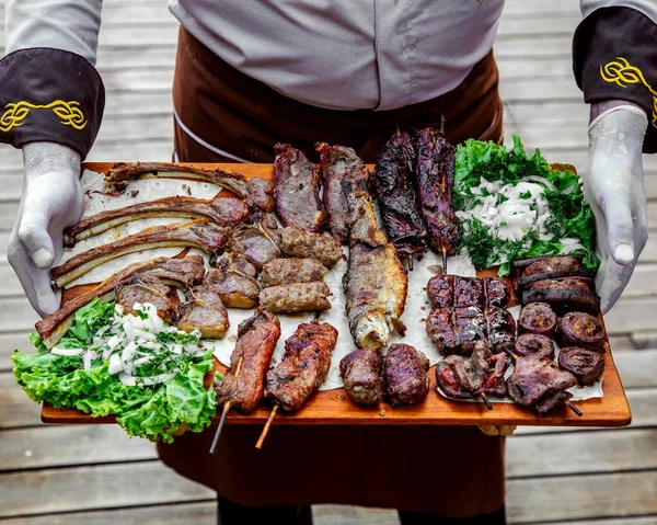 chef holding a platter of kebabs and grills with onion and herbs mixture