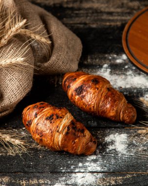Masanın üzerinde buğday ve un olan çikolatalı kruvasan.