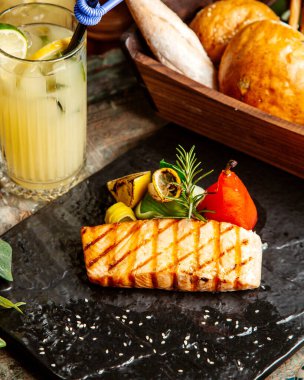 Izgara somon bifteği ızgara sebzeli limonlu biberiye ev yapımı limonata ve masada ekmek.