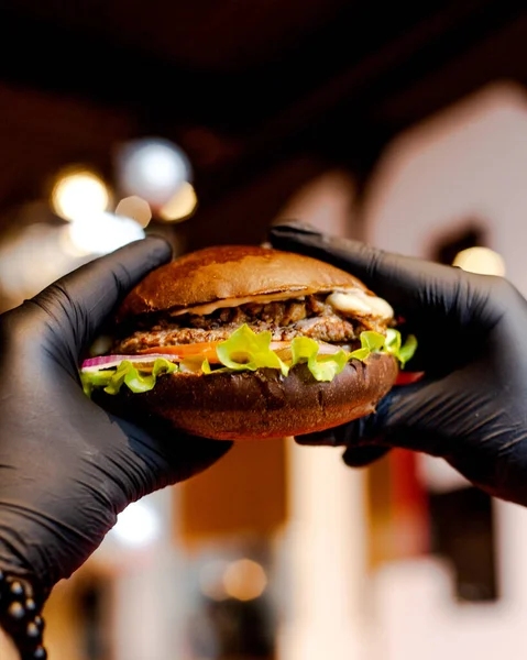 man with black burger gloves holds beef burger with brown bun