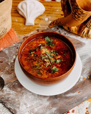 Kharçolu Gürcü çorbası, cevizli tkemali sosu ve kabın içinde yeşillikler.