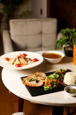 Salata, pilav ve sezar salatasıyla servis edilen tavuk bifteği.