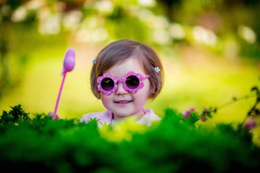 Pembe elbiseli, güneş gözlüklü, parkta yürüyen küçük, güzel bir kız.