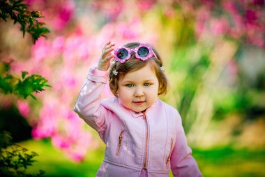 Pembe elbiseli, güneş gözlüklü, parkta yürüyen küçük, güzel bir kız.