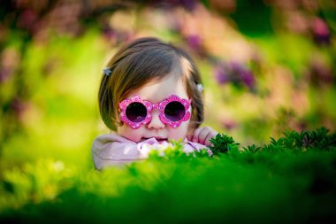 Pembe elbiseli, güneş gözlüklü, parkta yürüyen küçük, güzel bir kız.