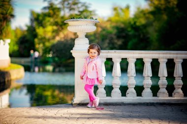 Mavi gözlü, küçük, güzel bir kız. Pembe elbisesiyle parkta yürüyor.