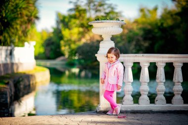 Mavi gözlü, küçük, güzel bir kız. Pembe elbisesiyle parkta yürüyor.