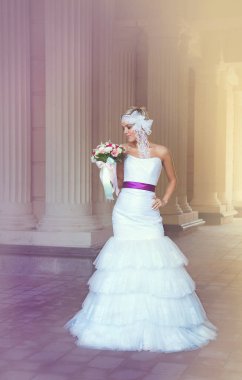 Güzel, genç bir gelin, eski moda bir elbise içinde, beyaz, elinde çiçeklerle poz veriyor.