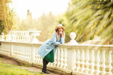 Güzel, genç bir kadın, mavi ceketli ve açık renk şapkalı, baharda, güneşli bir günde parkta yürüyen.