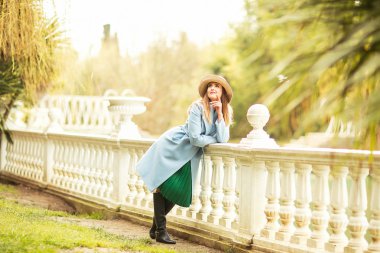 Güzel, genç bir kadın, mavi ceketli ve açık renk şapkalı, baharda, güneşli bir günde parkta yürüyen.