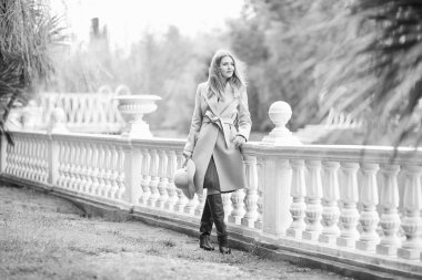 Güneşli bir günde, çiçek açan bir manolya ağacının yanında parka yürürken, şık bir ceket ve şapkayla genç, güzel bir kadının siyah ve beyaz fotoğrafı.