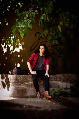 Uzun saçlı, kahverengi gözlü genç ve yakışıklı bir adam sokakta parlak bir gömlek ve siyah kot pantolonla yürüyor.