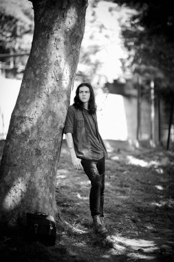 Siyah-beyaz bir fotoğraf, uzun, siyah saçlı, kahverengi gözlü, çilli bir yüz, şık bir gömlek ve kot pantolon içinde, üzgün bir ruh hali içinde caddede yürüyor.