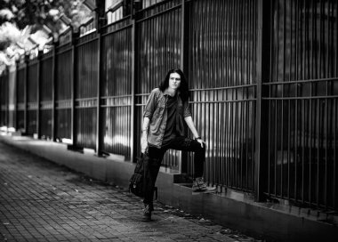 Siyah-beyaz bir fotoğraf, uzun, siyah saçlı, kahverengi gözlü, çilli bir yüz, şık bir gömlek ve kot pantolon içinde, üzgün bir ruh hali içinde caddede yürüyor.