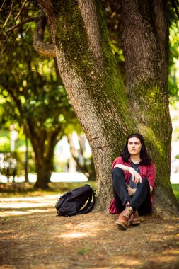 Siyah, uzun saçlı, kahverengi gözlü genç, yakışıklı bir adam yazın parkta yürür.