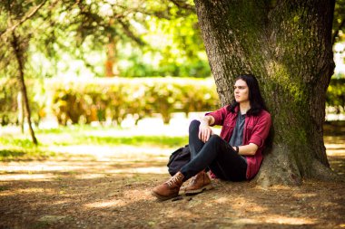 Siyah, uzun saçlı, kahverengi gözlü genç, yakışıklı bir adam yazın parkta yürür.