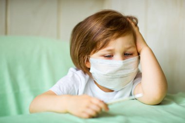 Küçük bir kız, tıbbi maske takıyor, evde oynuyor, karantinada, koronavirüs salgını sırasında, COVID-2019