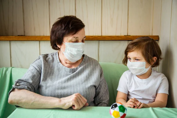 an adult woman, a retired grandmother, with a granddaughter , and wearing a medical mask, is in home quarantine, and playing because of COVID-19