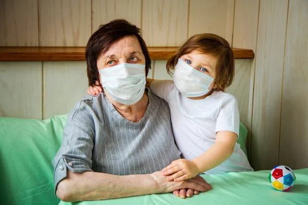 Yetişkin bir kadın, emekli bir büyükanne, torunu var ve tıbbi maske takıyor. Ev karantinasında ve COVID-19 yüzünden oynuyor.