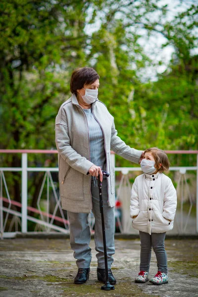 Tıbbi maskeler takan bir kız ve büyükannesi COVID-19 salgını sırasında ıssız bir sokakta yürüyorlar.