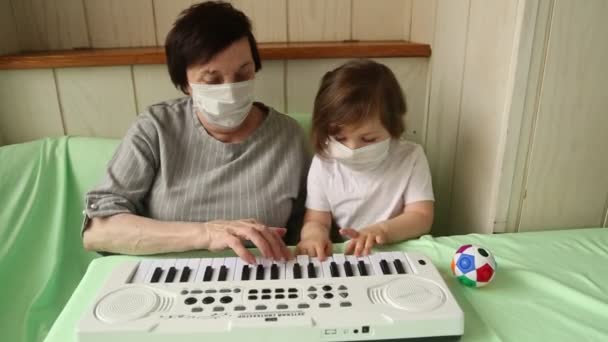 Een volwassen vrouw, met een klein meisje, die piano leert spelen, tijdens een thuisquarantaine, als gevolg van de hevige-19 pandemie — Stockvideo