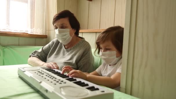 한 성인 여성 이 어린 소녀와 함께 집에 격리되어 있는 동안 피아노를 배우고 있습니다. — 비디오
