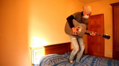 Karantina sırasında tıbbi maskeli bir adam, covid-2019 salgınından dolayı gitar çalar.