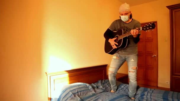Человек в медицинской маске играет на гитаре во время карантина из-за пандемии ковида-2019 — стоковое видео