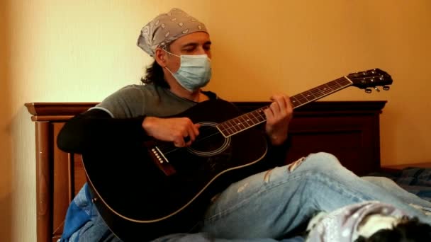 Un uomo in maschera medica suona la chitarra, durante la quarantena, a causa della pandemia covid-2019 — Video Stock