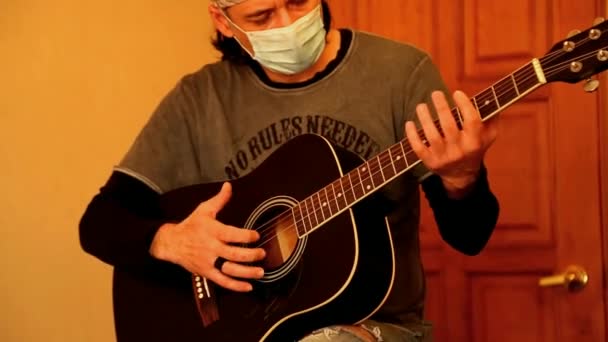 Um homem com uma máscara médica toca guitarra, durante a quarentena, devido à pandemia de covid-2019 — Vídeo de Stock