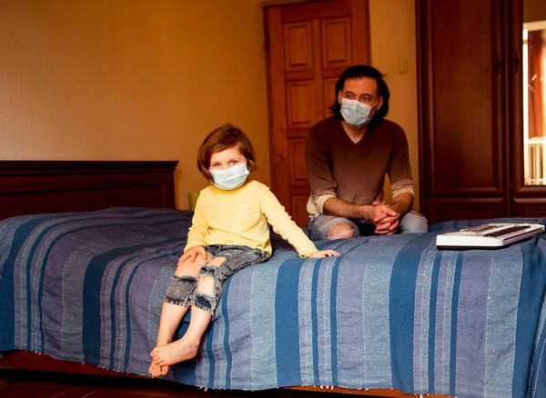 dad and daughter in a medical mask, sitting at home in quarantine, and the two of them play, because of the covid-19 pandemic