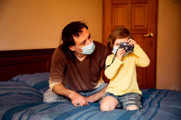 daddy and daughter in medical masks, studying art photography, at home during quarantine, due to the covid-19 pandemic