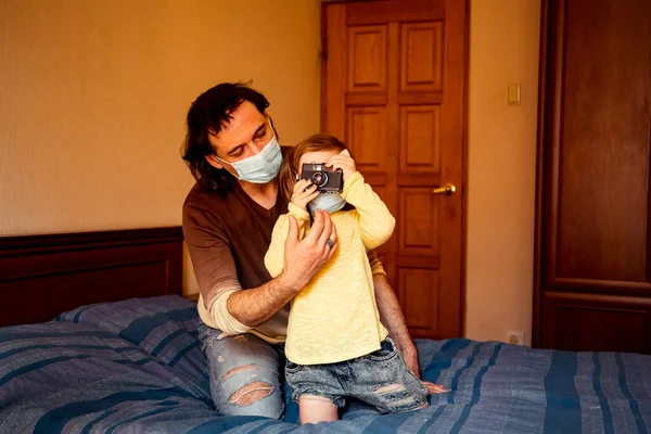 daddy and daughter in medical masks, studying art photography, at home during quarantine, due to the covid-19 pandemic