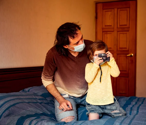 daddy and daughter in medical masks, studying art photography, at home during quarantine, due to the covid-19 pandemic