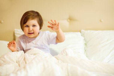 Mavi gözlü tatlı küçük bir kız, beyaz bir yatakta karantina altında yatıyor, çünkü covid-19 salgını var.